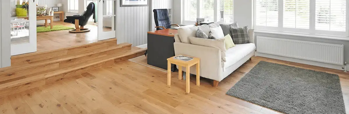 A modern living room with professionally installed laminate flooring, a beige sofa, a small side table, a gray rug, and large windows with white shutters in Phoenix, AZ